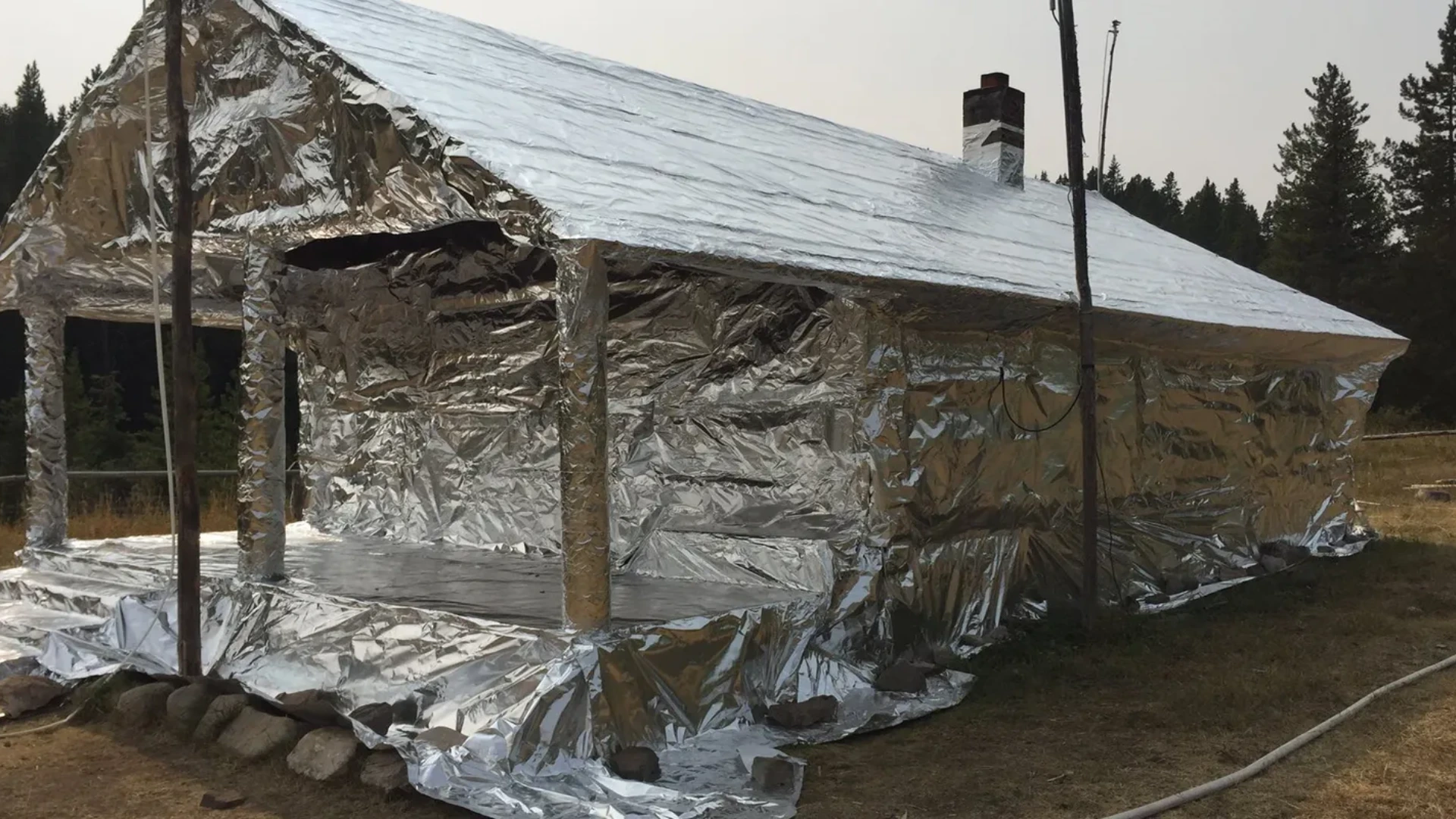 Cabin completely wrapped in FireFoil protective material in forest setting
